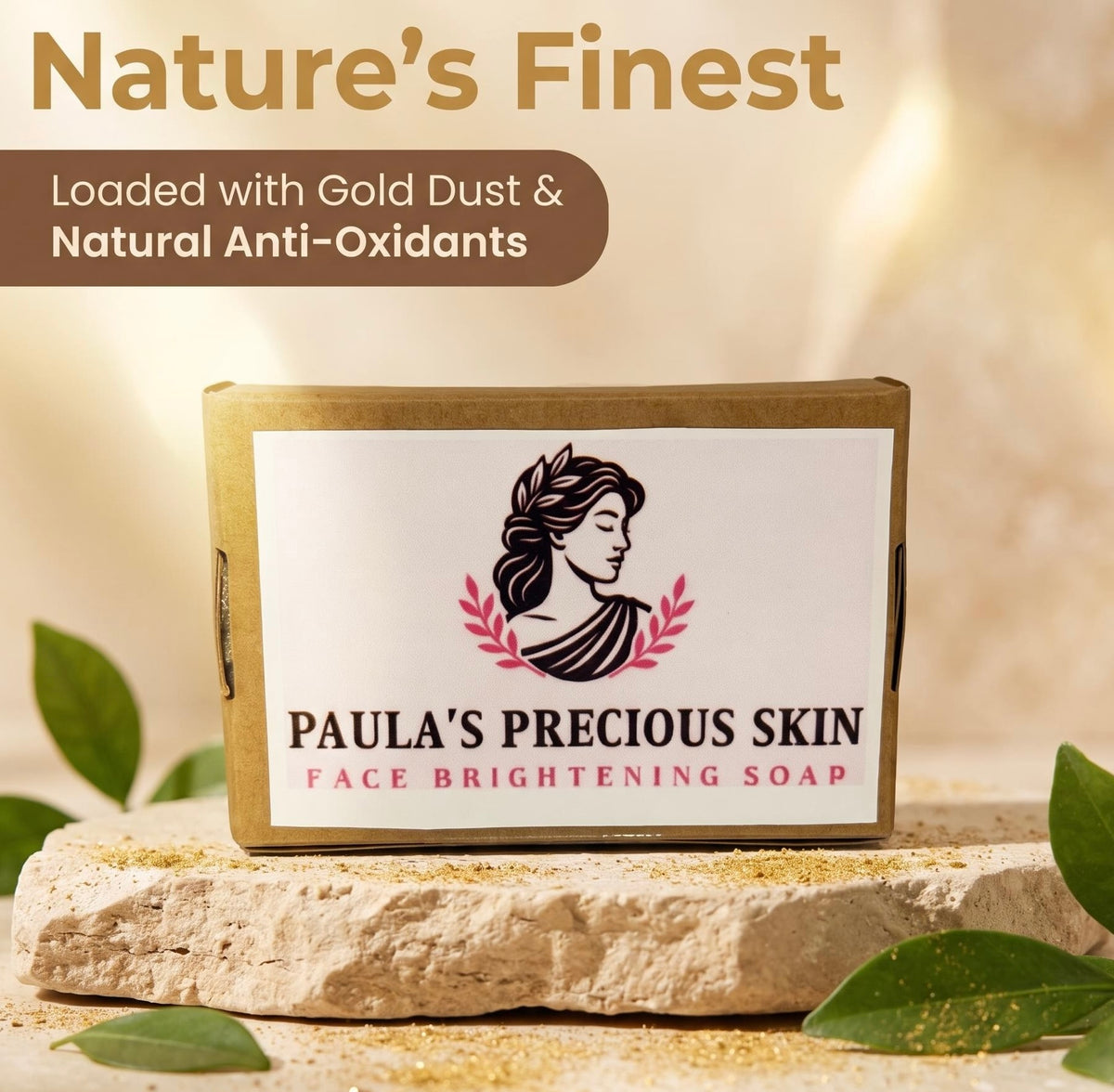 A rectangular box of Paula's Precious Skin Face Brightening Soap sits on a stone slab with green leaves around it. The box is gold-toned with a white front label featuring a black profile illustration and pink decorative text.