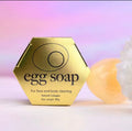 Gold hexagonal egg soap packaging with a soft focus background