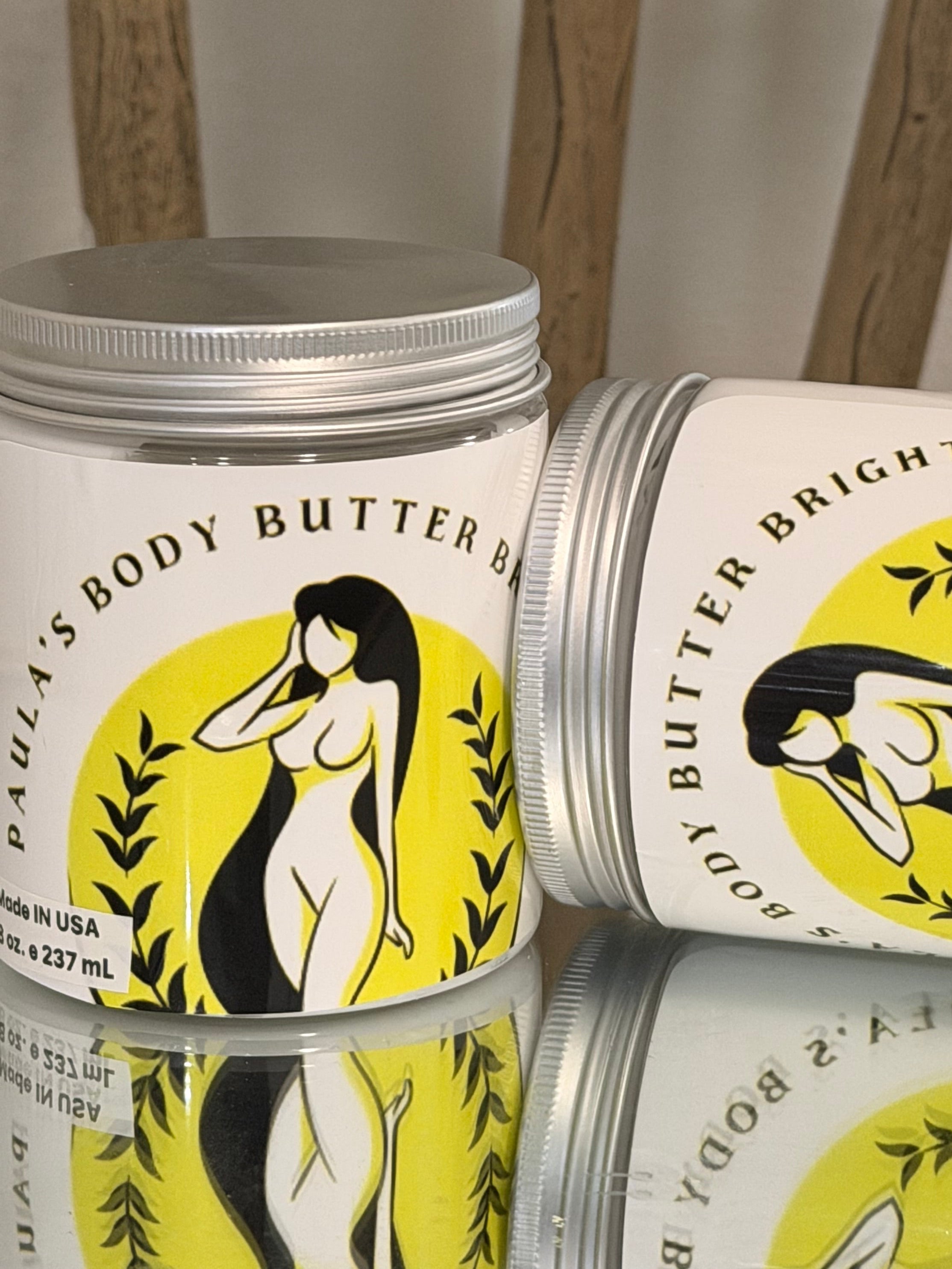 Body butter tins with a yellow and black label on a neutral background