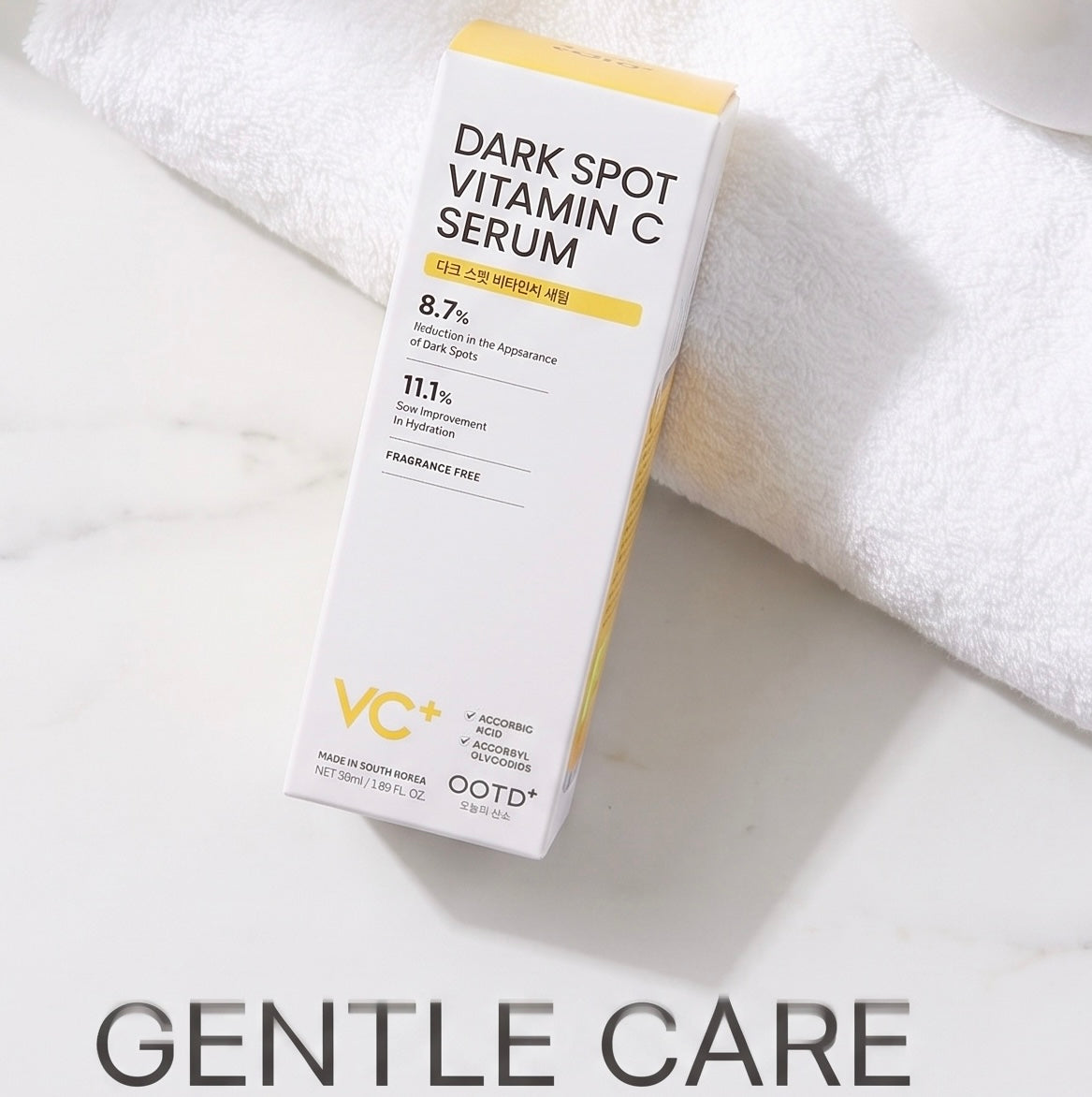 A boxed skincare product labeled 'DARK SPOT VITAMIN C SERUM' by OOTD+ is photographed on a white marble surface with a folded white towel behind it. The box is mostly white with yellow accents and black text.
