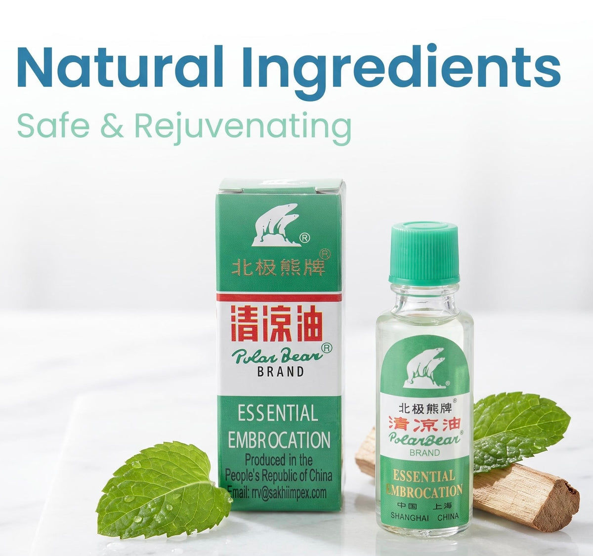 Polar Bear Brand Essential Embrocation oil bottle and its green-and-white box, styled with mint leaves and small wood pieces on a white surface, with the text 'Natural Ingredients Safe & Rejuvenating' at the top.
