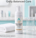 A bottle of Acne Foaming Face Wash by Paula, labeled as a gentle cleanser, displayed on a marble countertop with a white towel and a glass beaker in a bright bathroom setting. Text overlays read 'Daily Balanced Care' and 'Removes excess sebum'.