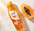 A bottle of PAW PAW Papaya Boiling Clamperat hair gel lies on a light marble surface next to a halved papaya, with a few water droplets nearby.
