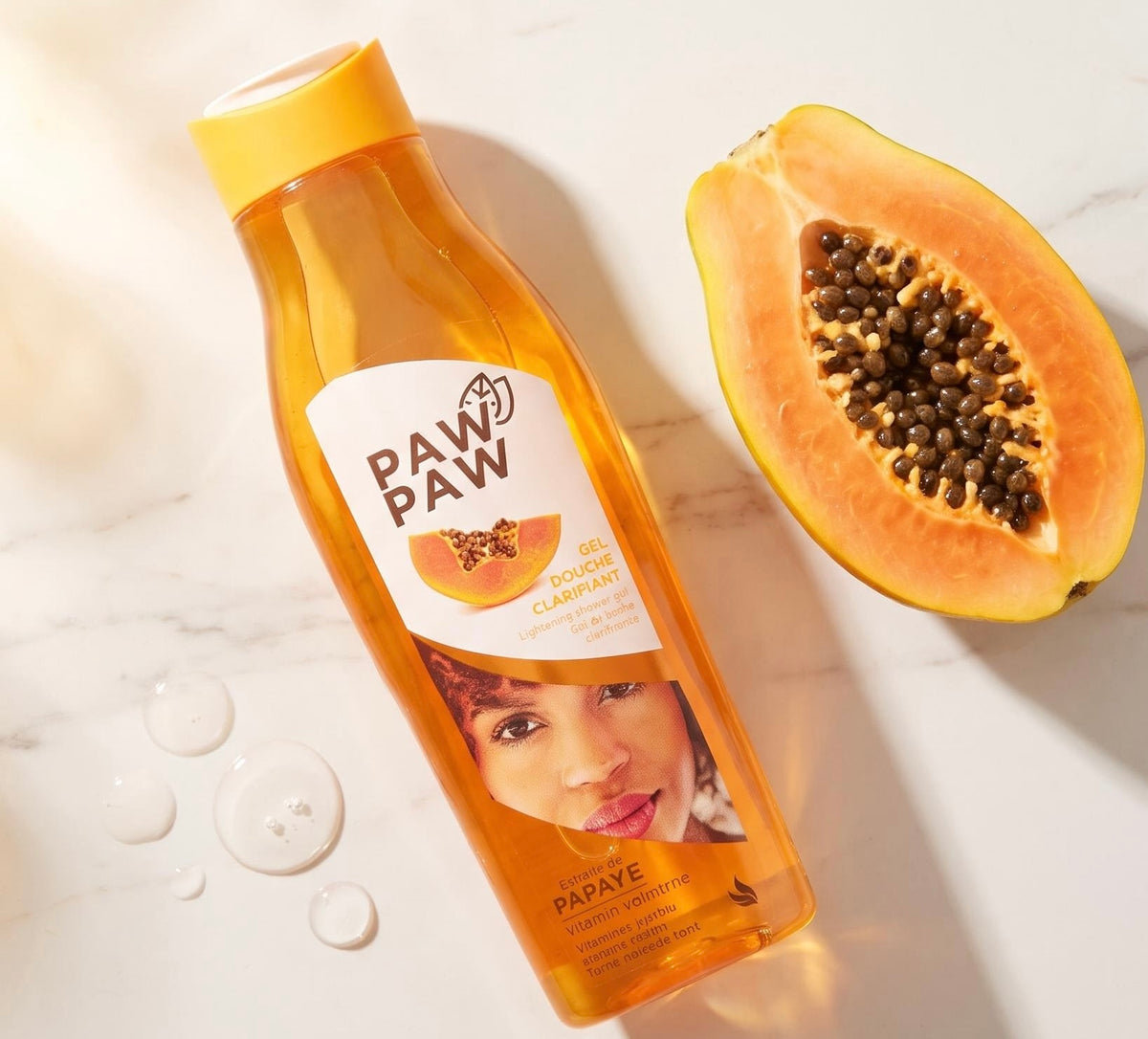 A bottle of PAW PAW Papaya Boiling Clamperat hair gel lies on a light marble surface next to a halved papaya, with a few water droplets nearby.