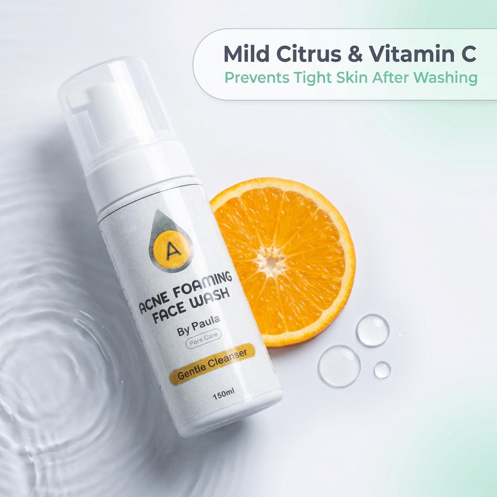 A bottle of acne foaming face wash by Paula, styled with a sliced orange and water droplets on a light background with text overlay.