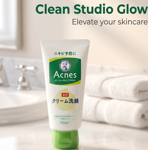 A tube of Rinsel Acnes cream facial cleanser standing on a bathroom counter with a sink and folded towels blurred in the background. The product packaging is white with green and yellow accents, and the text 'Clean Studio Glow' is visible at the top.