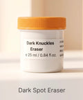 A white cosmetic jar with an orange lid labeled 'Dark Knuckles Eraser' on a warm beige background, with the text 'Dark Spot Eraser' below.