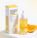 VC+ Dark Spot Vitamin C Serum shown with its white and yellow retail box and a clear dropper bottle filled with golden-yellow serum, styled with orange slices on a clean white background.