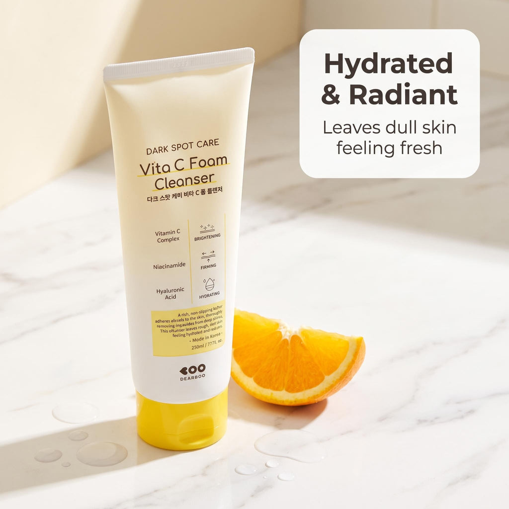 A tube of EOO Beauty Vita C Foam Cleanser stands on a light marble surface next to an orange slice, with a text overlay reading 'Hydrated & Radiant Leaves dull skin feeling fresh'.