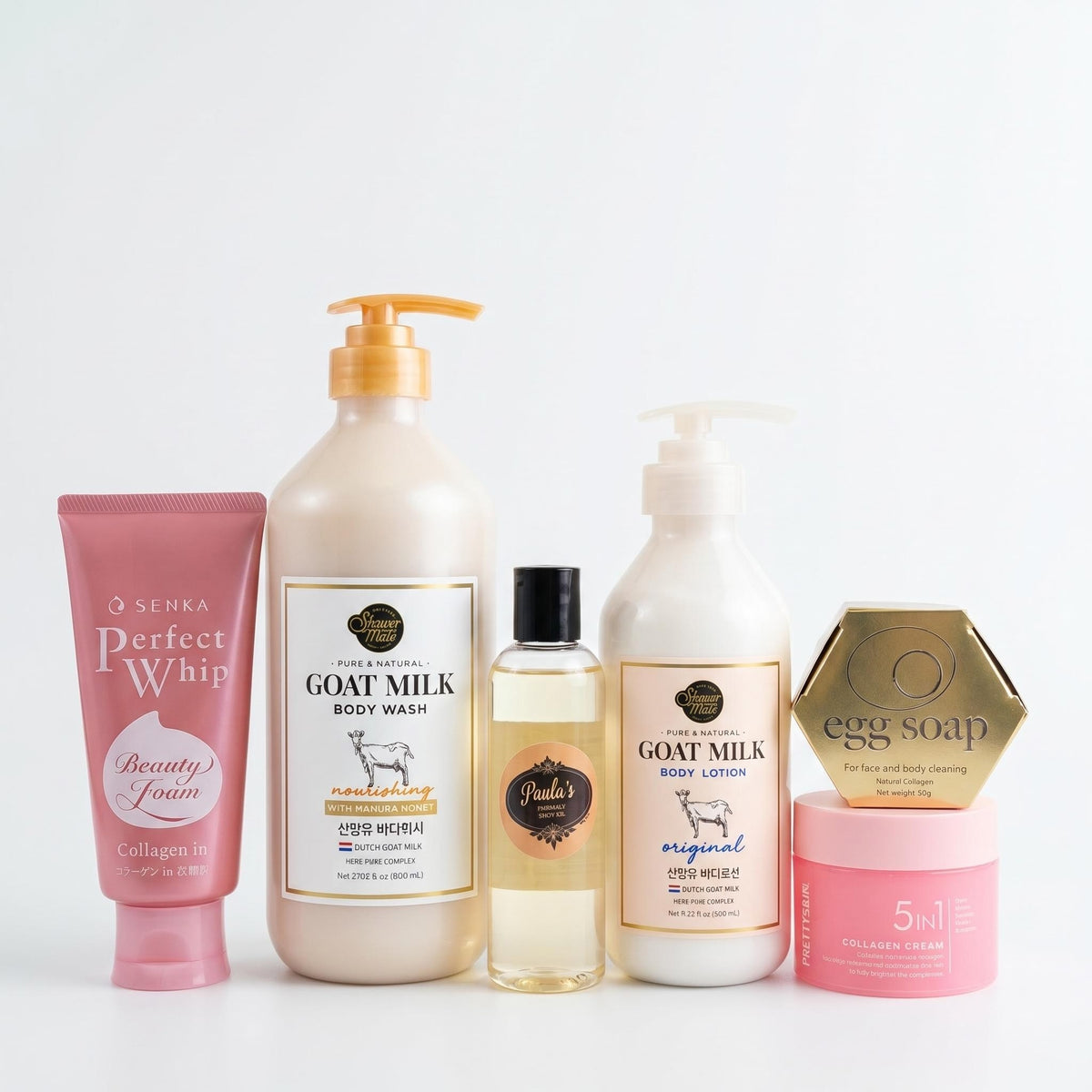 A group of six personal care products from the brand O Senka arranged on a clean white background. The products include a pink tube of Perfect Whip Beauty Gooz, a large beige bottle of Goat Milk Body Wash, a small amber bottle of Handmade Body Lotion, a white pump bottle of Goat Milk Body Lotion, a pink jar of Collagen Cream, and a gold hexagonal box of Egg Soap.