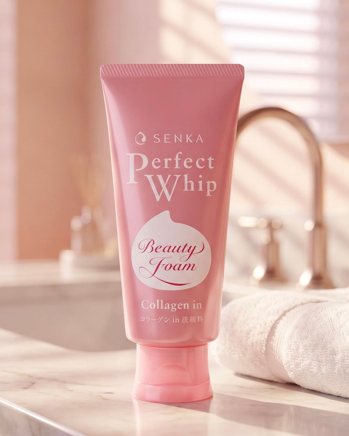 A pink squeeze tube of Senka Perfect Whip Beauty Foam Collagen in foam, standing on a marble countertop with a blurred bathroom sink and faucet in the background.