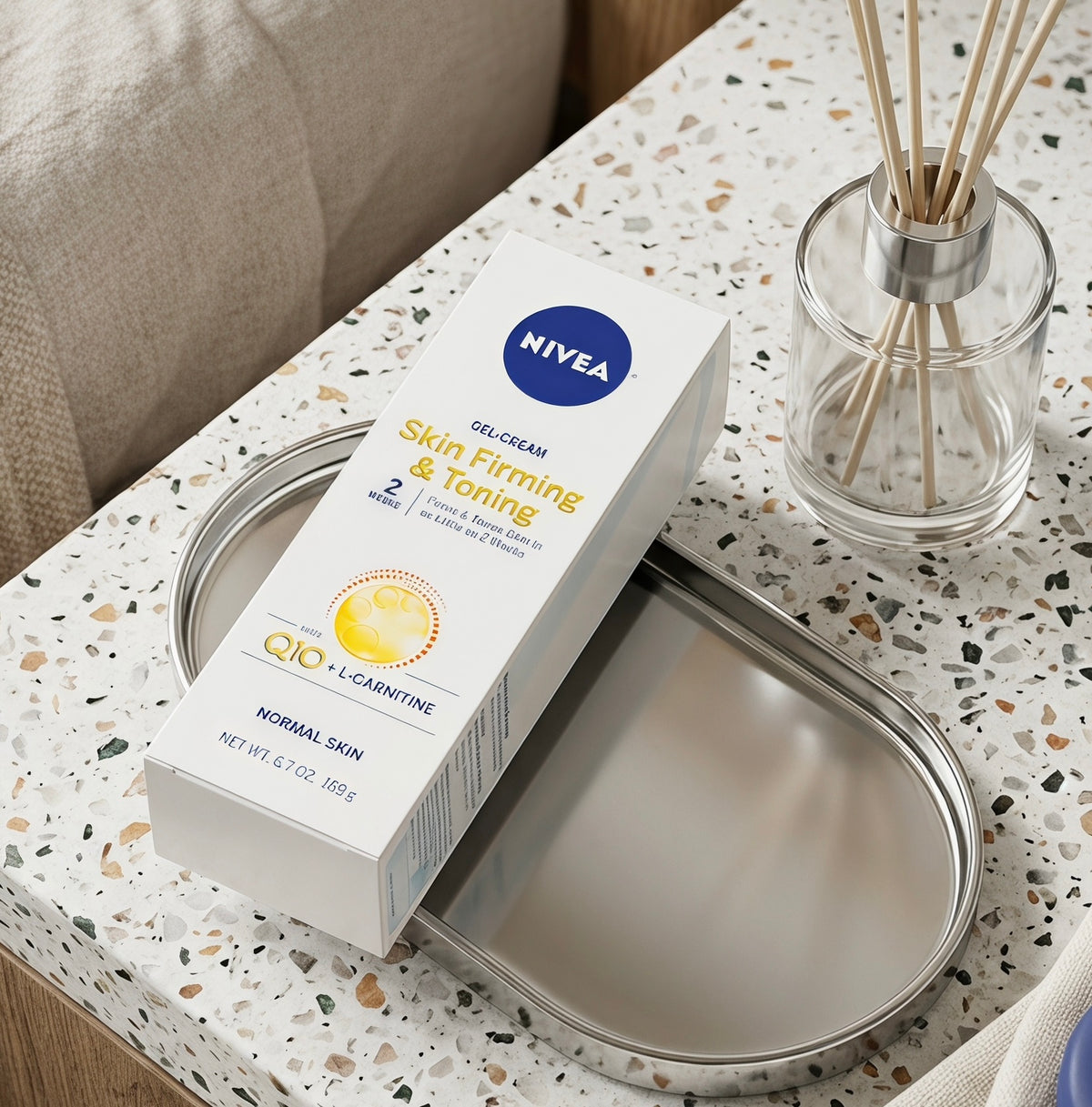 NIVEA Skin Fitting & Toning Gel Cream box placed on a silver oval tray on a speckled terrazzo tabletop, with a glass reed diffuser nearby.