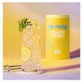 Glass of lemonade with ice and a container of Vital Proteins Collagen Peptides Lemon flavor on a yellow background.
