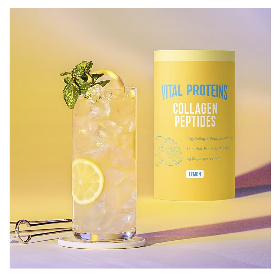 Glass of lemonade with ice and a container of Vital Proteins Collagen Peptides Lemon flavor on a yellow background.